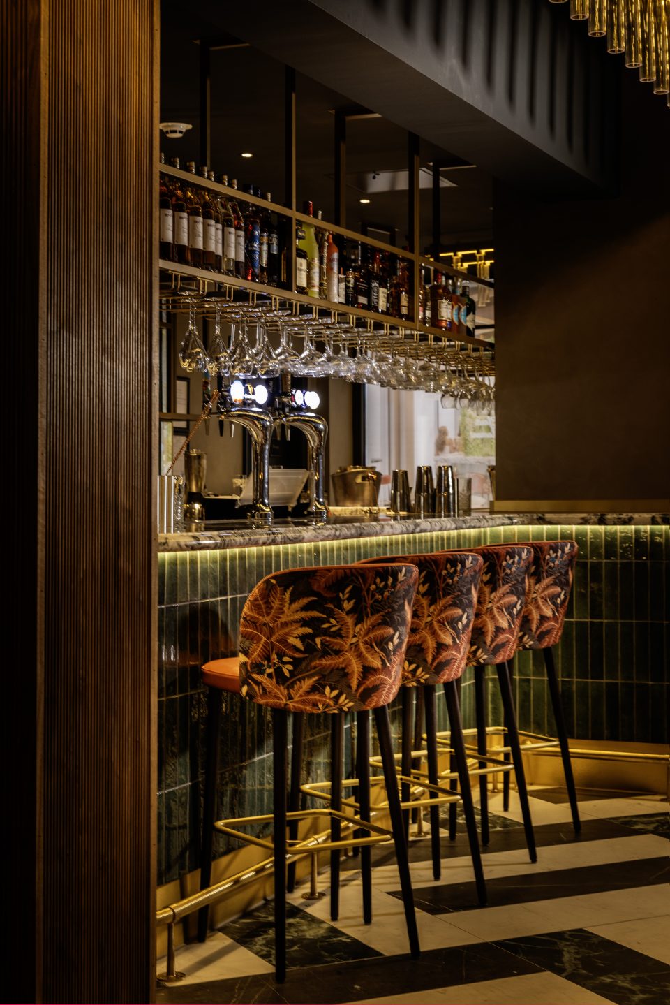 A picture of four bar stools aligned at the bar with hanging glasses above