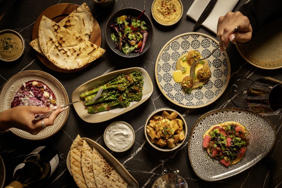 A bird's eye view of a table, with several plates of bread, broccoli and salad.