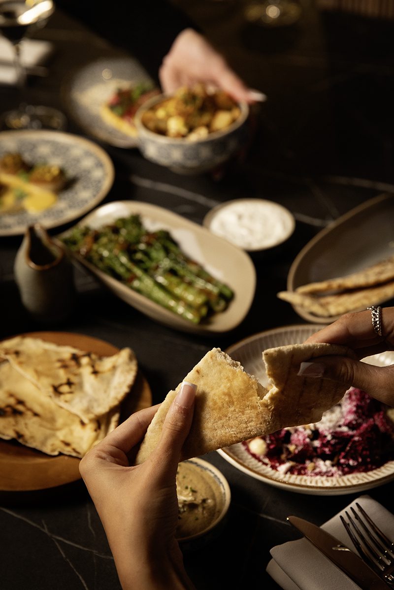 A pair of hands tearing a piece of flatbread with a series of small plates blurred in the background